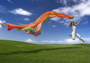 Mujer saltando con una bandera al viento, simbolizando energía, libertad y bienestar empresarial.