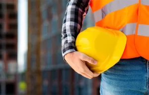 Trabajador con chaleco de seguridad sosteniendo casco, representando los riesgos laborales y a cuidarnos a nosotros mismos.